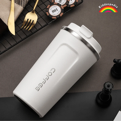 White coffee tumbler on a dark surface with gaming pieces and a rainbow logo in the corner.
